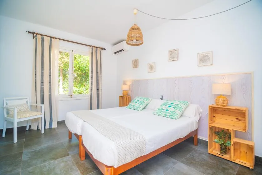 A bright bedroom with a double bed, bedside tables, and a window overlooking greenery.