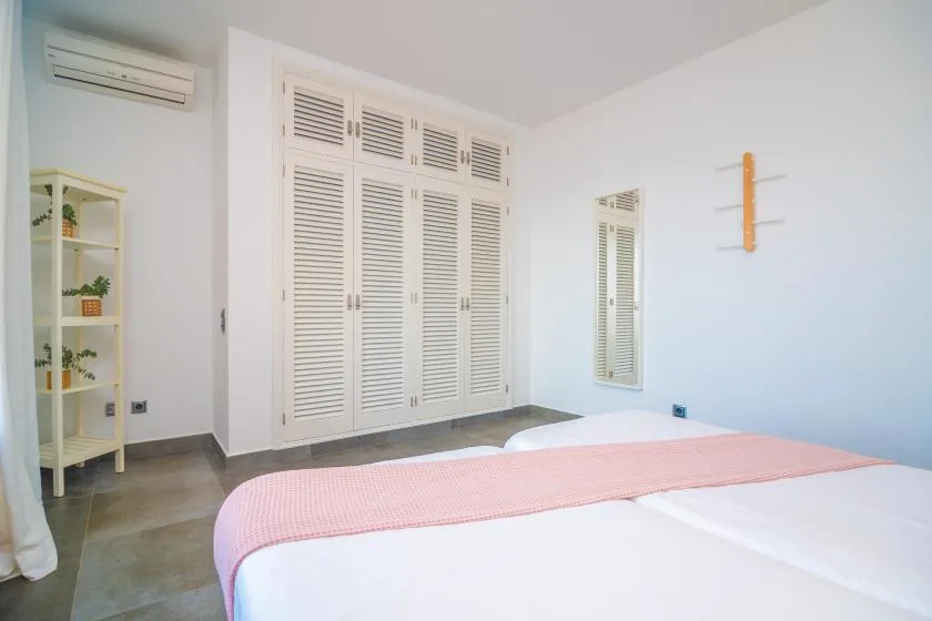 A bedroom with a bed, white louvered closet doors, and a small wall mirror.