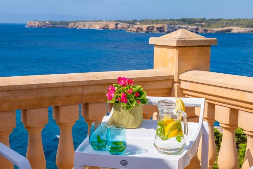 A seaside terrace with a table holding flowers, drinks, and a pitcher.