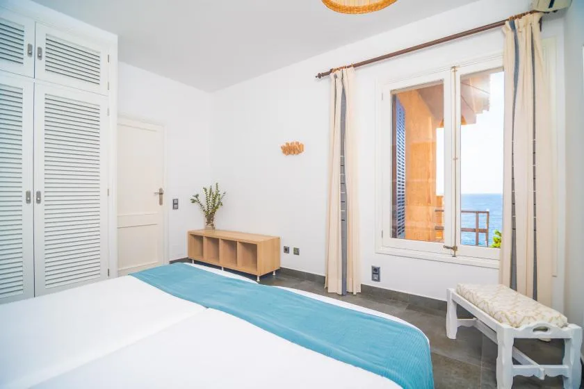 A bedroom with a bed beside a large window overlooking the water.