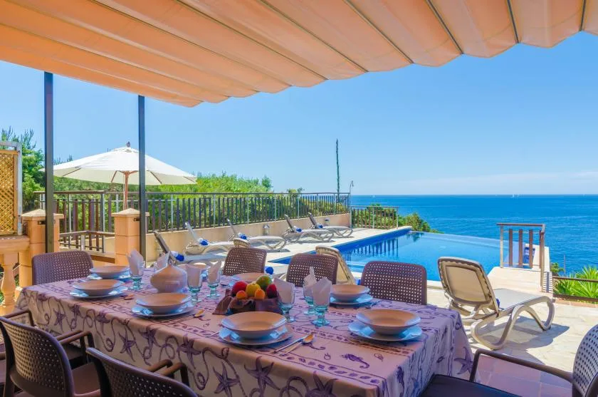 Una mesa de comedor al aire libre está junto a una piscina con vistas al mar.