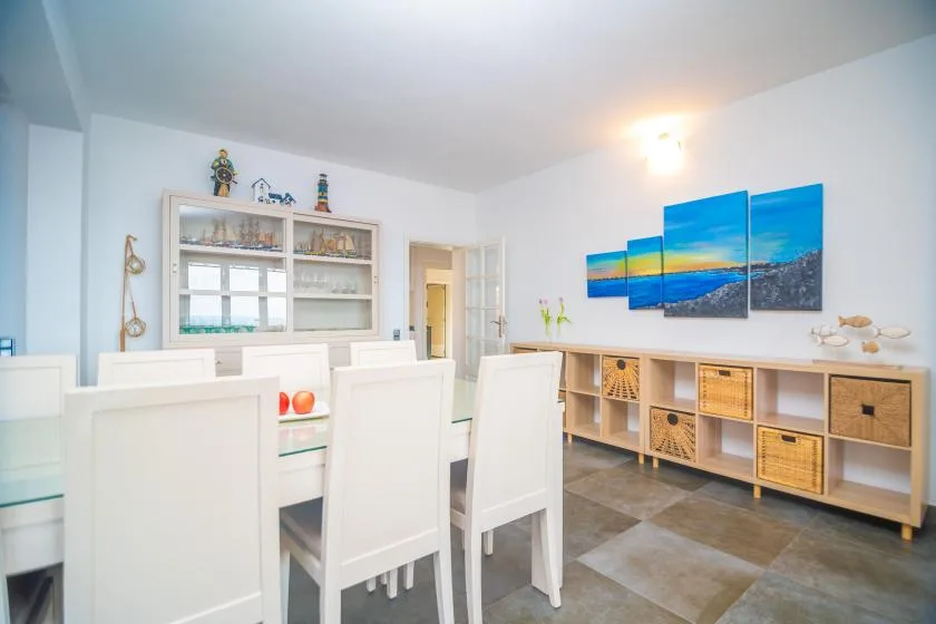 A bright dining area with white seating and a long wooden storage unit.
