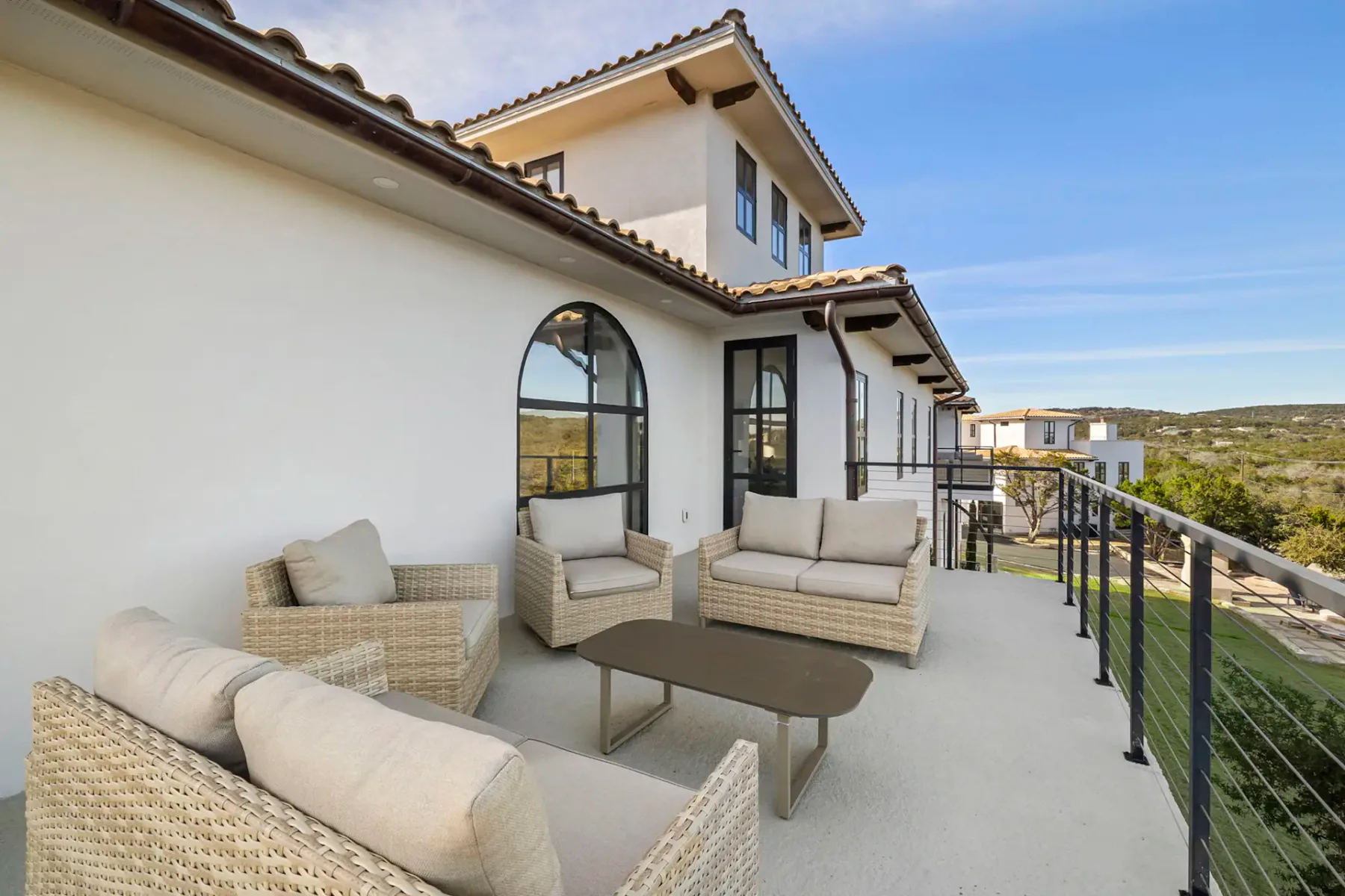 Outdoor patio with woven seating and a railing overlooking a hillside.
