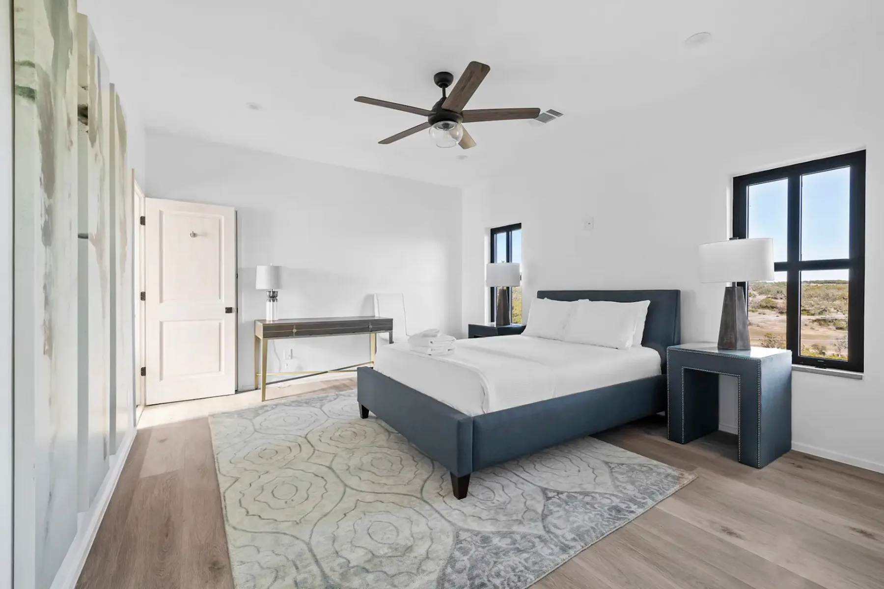 A bright bedroom with a large bed, a ceiling fan, and windows.