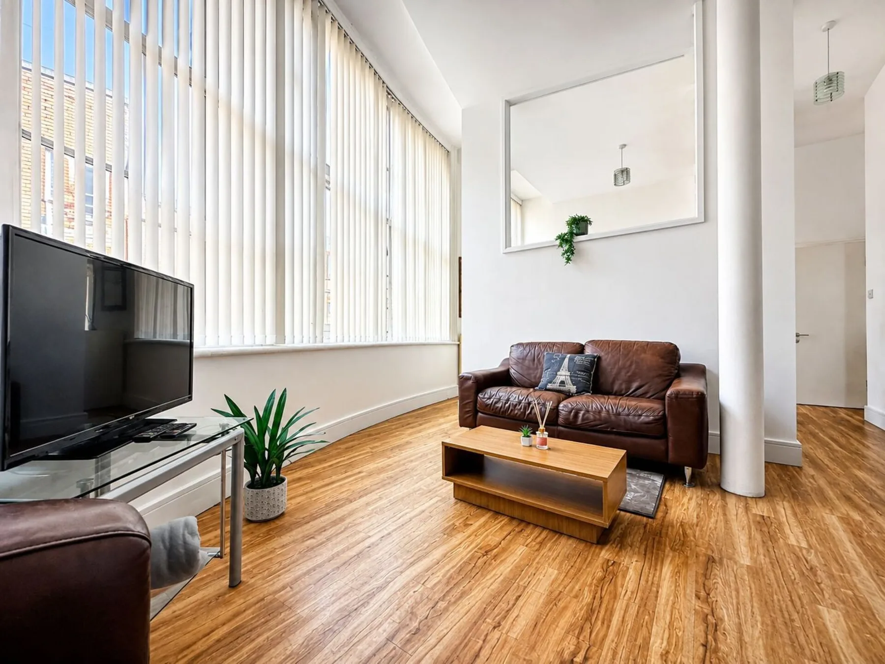 A bright living room with leather seating, a coffee table, and tall windows.