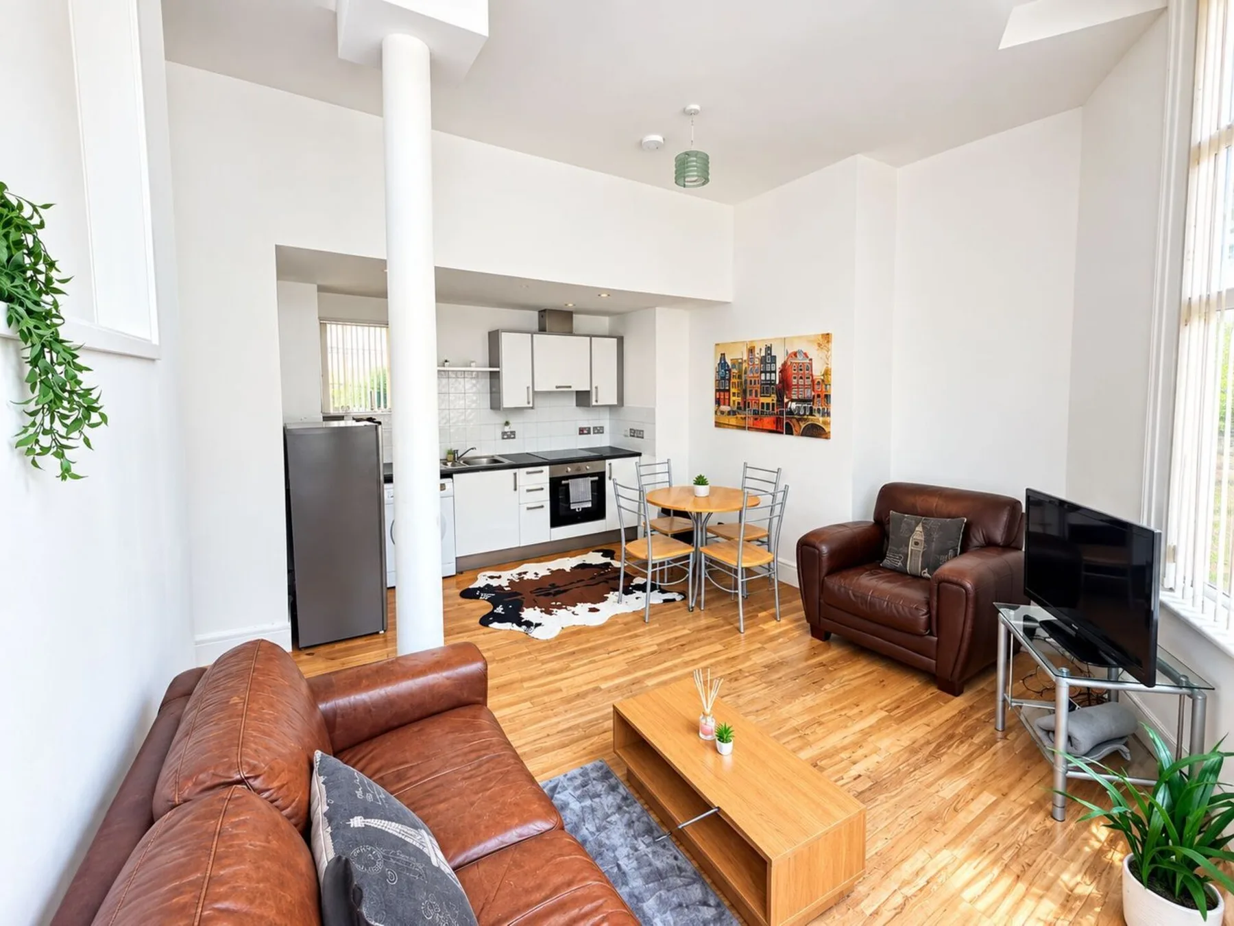 Sala de estar con asientos, un televisor y una cocina abierta.