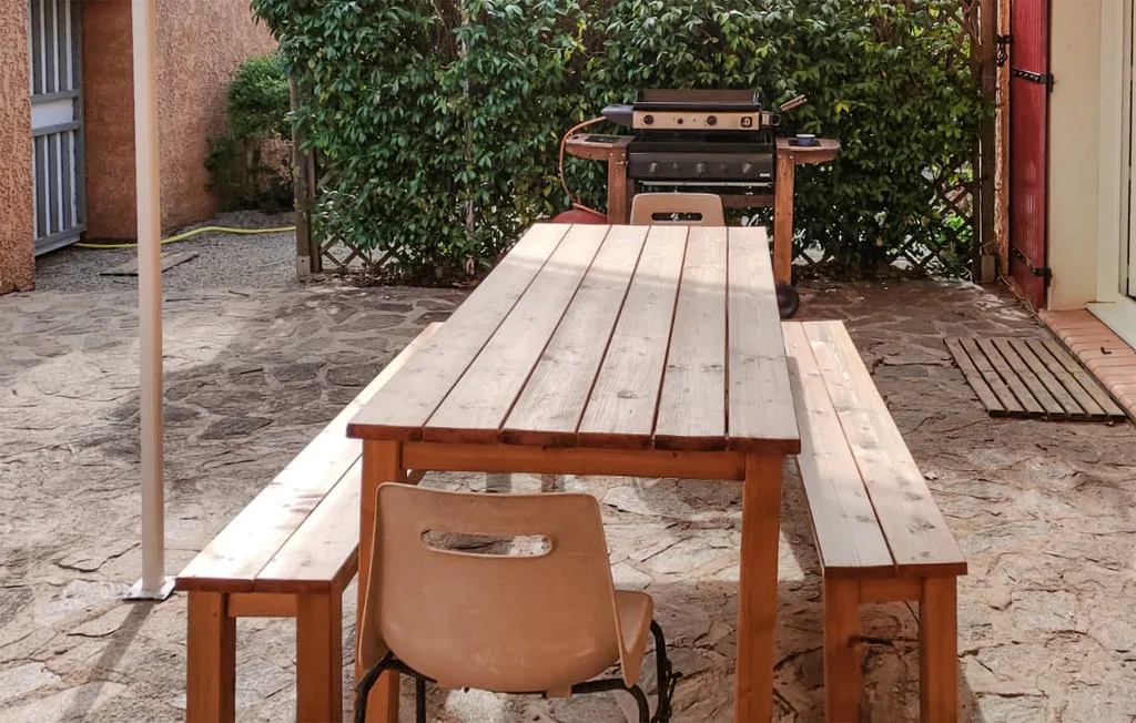 Una mesa de comedor al aire libre con bancos está frente a una parrilla.