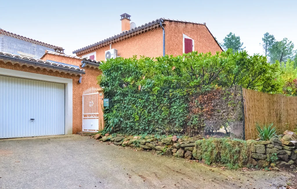 Una casa y un garaje están detrás de un seto frondoso junto a una entrada pavimentada.