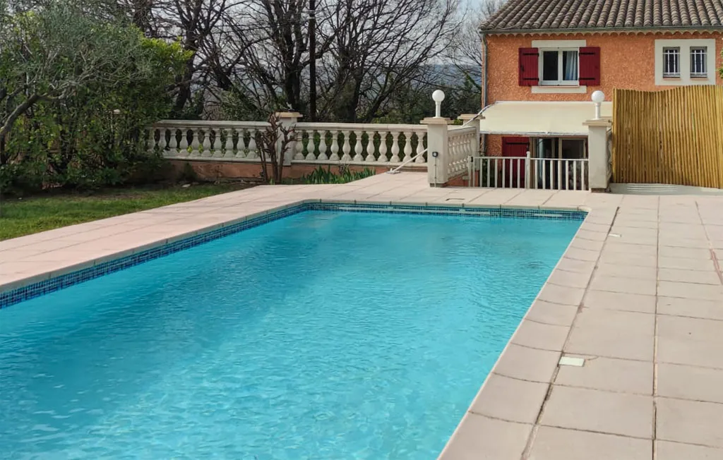 An outdoor swimming pool beside a paved patio and a house.