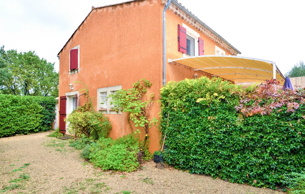 Una casa naranja está junto a un camino de grava, con setos y un toldo exterior.