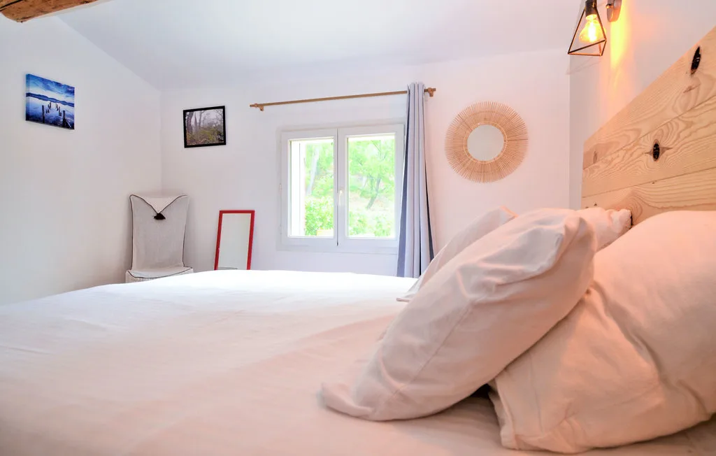 Un dormitorio luminoso con una cama, ropa de cama clara y una ventana con vistas a la vegetación.