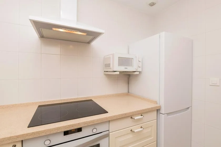 A bright kitchen with a cooktop, range hood, microwave, and refrigerator.