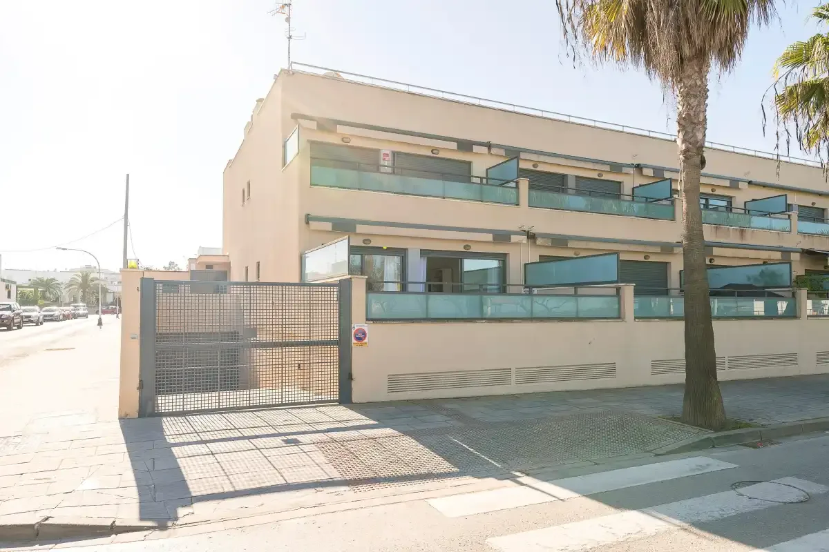 A modern multi-story building stands behind a metal gate on a sunny street.
