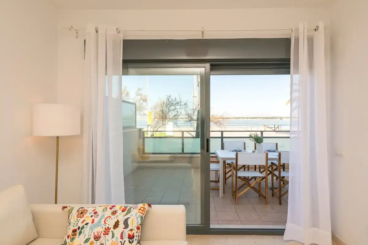 A bright living area opens onto a balcony with a dining table and chairs.