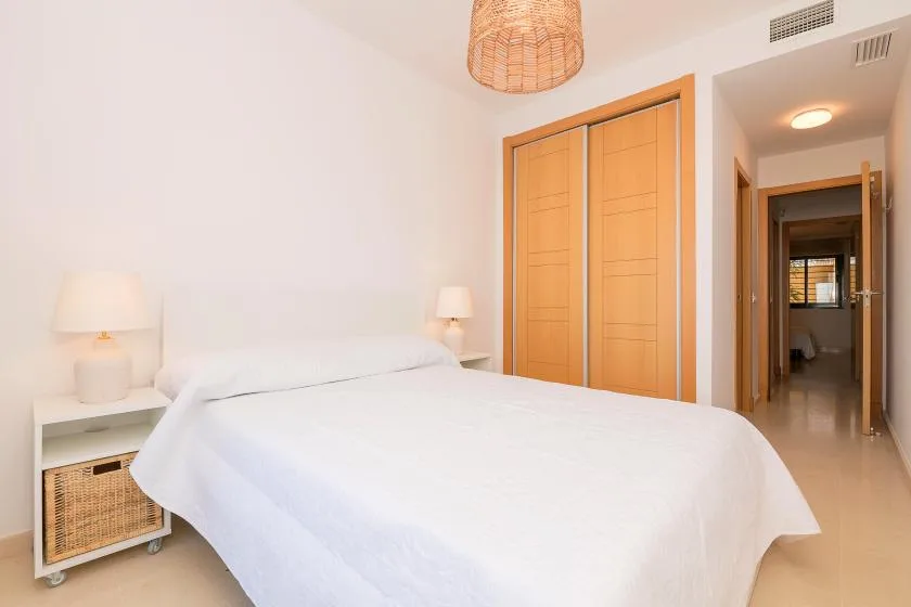 A bright bedroom with a large bed, bedside lamps, and wooden closet doors.