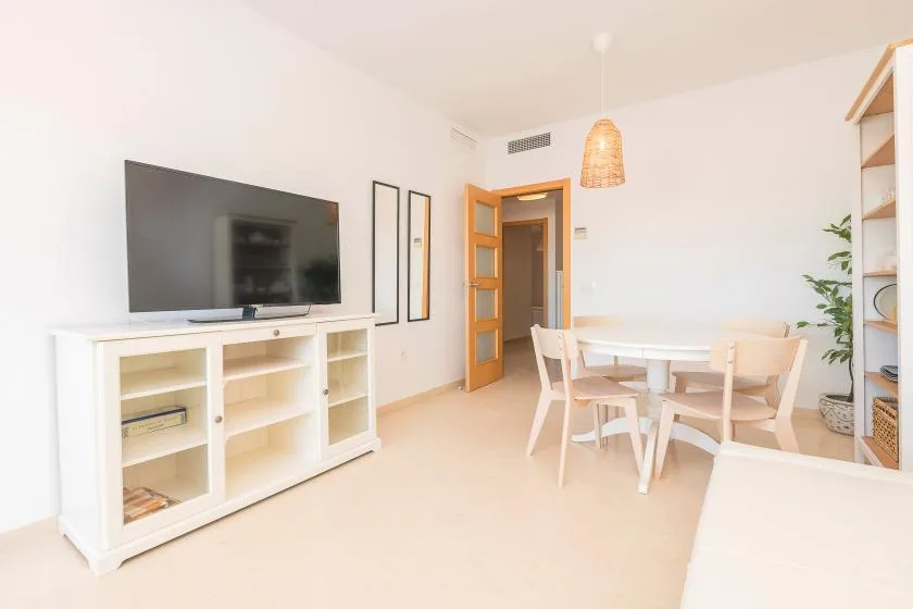 A bright dining and living area with a table, seating, and television.
