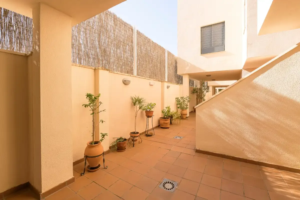 A sunlit tiled courtyard with potted plants and a staircase.