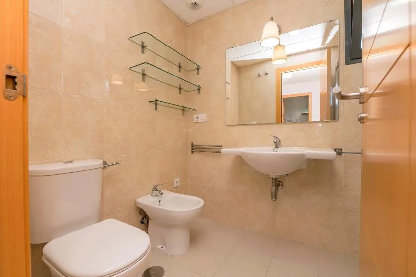 A tiled bathroom with a sink, mirror, toilet, and bidet.