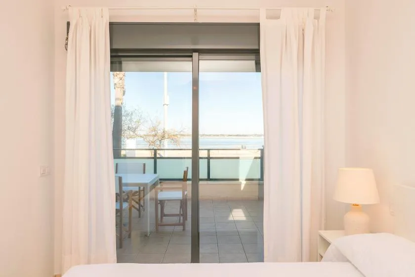 A bedroom opens through sliding glass doors onto a balcony overlooking the water.