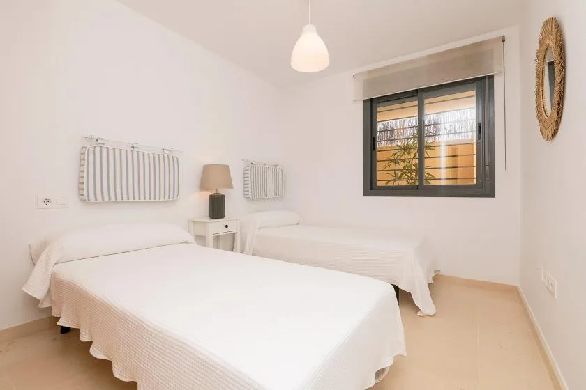 A bright bedroom with two beds and a window overlooking greenery.