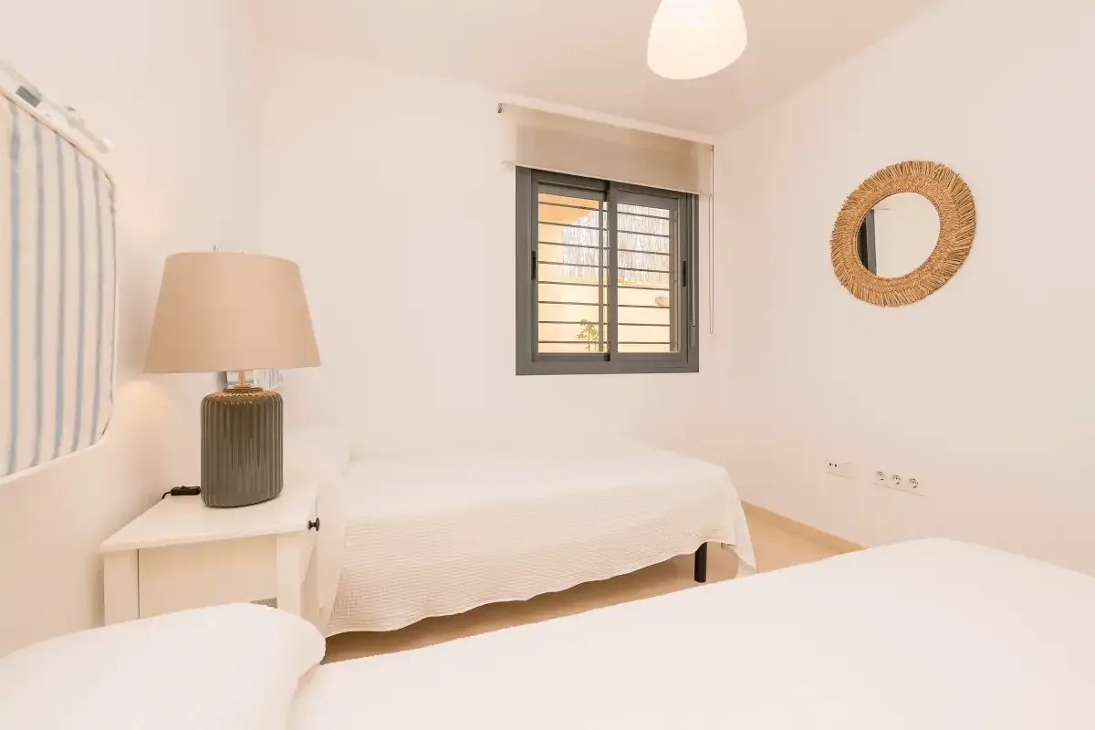 A bright bedroom with two beds, a bedside table, and a window.