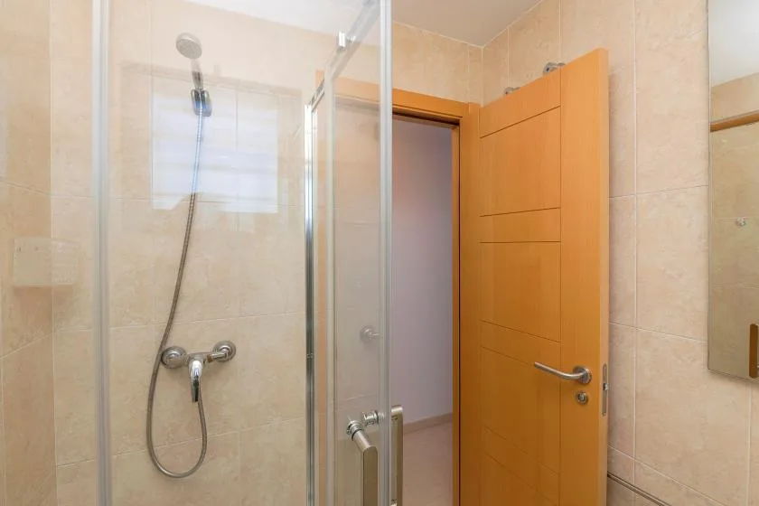 A tiled bathroom with a glass shower and an open wooden door.