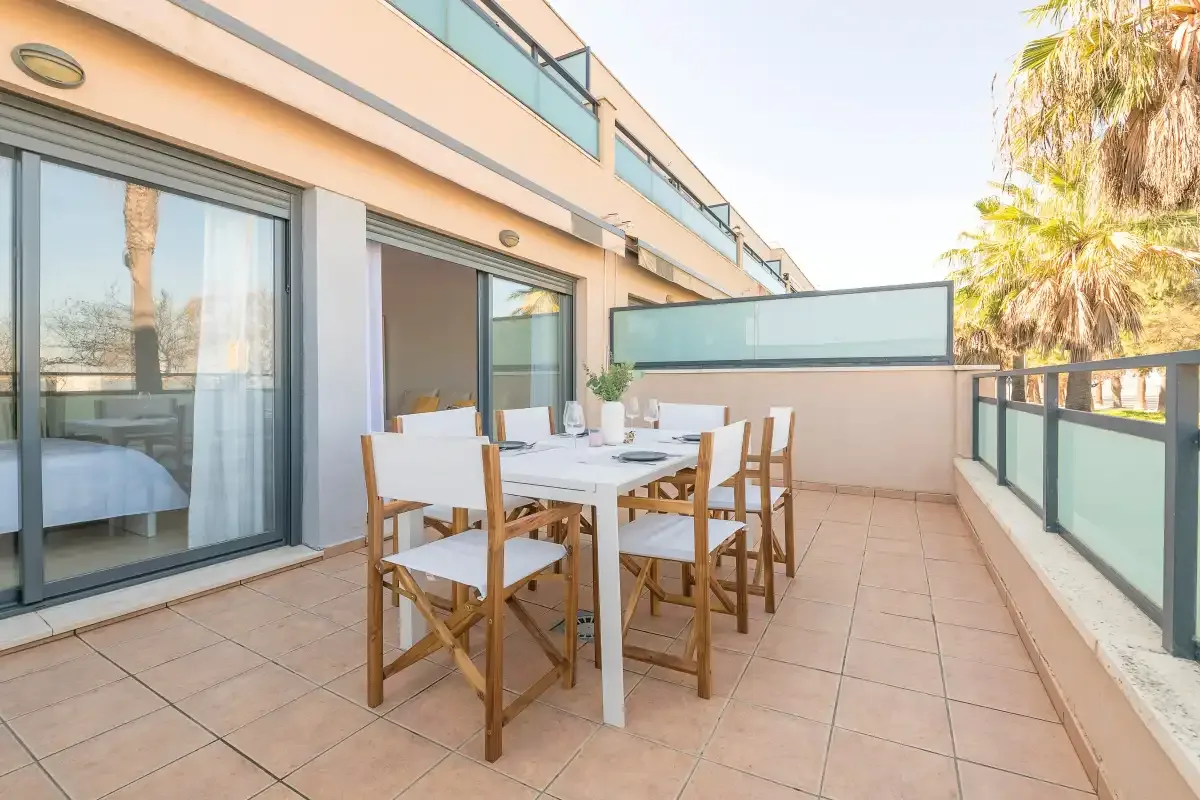 A tiled balcony has an outdoor dining table and seating beside glass doors.