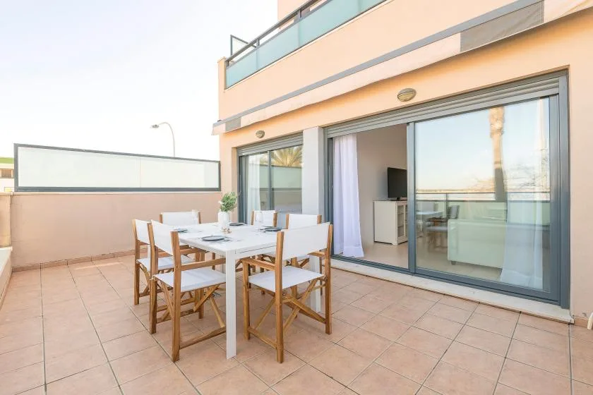 A tiled terrace with an outdoor dining table beside wide glass doors.