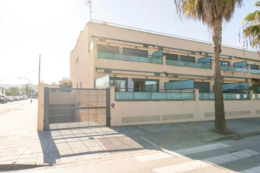 A modern multi-story building with glass balcony railings stands beside a gated sidewalk.