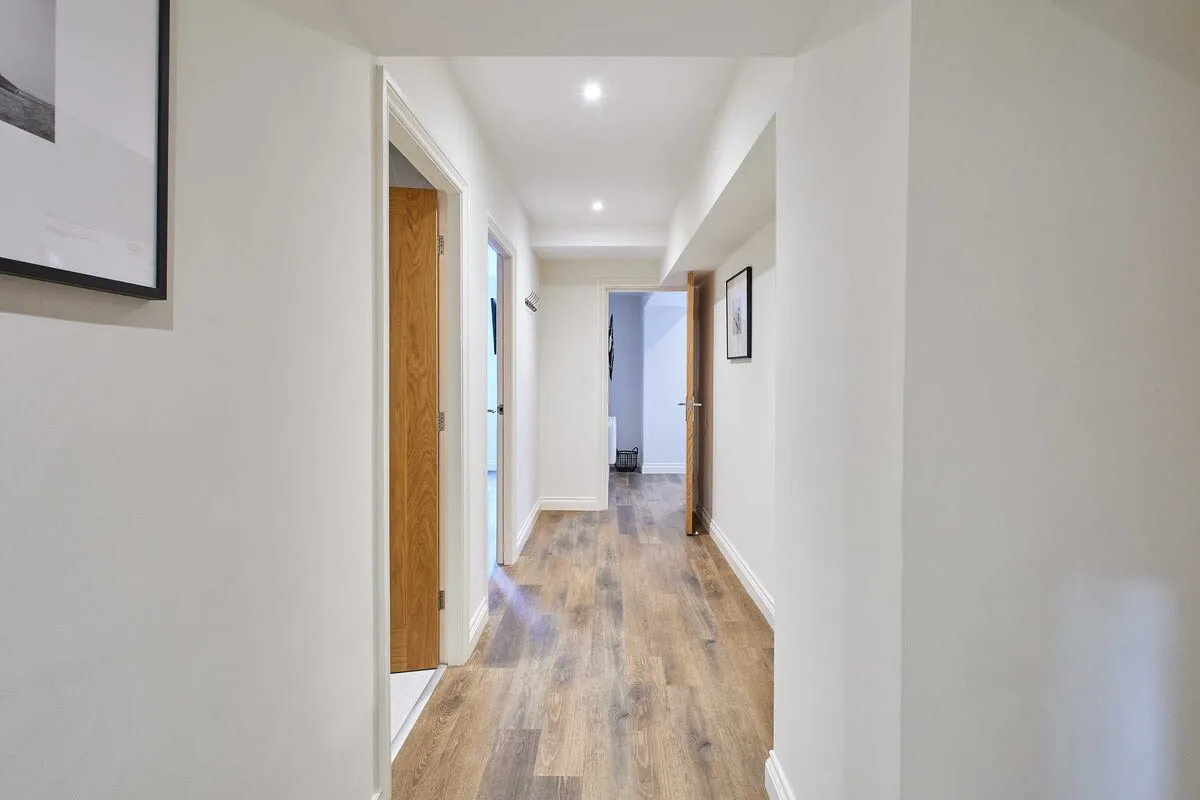 A bright hallway with wood flooring and doors along the walls.