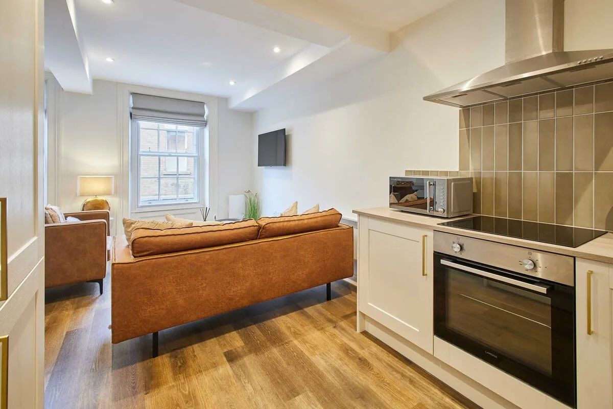 An open-plan living area and kitchen, with a brown sofa facing a wall-mounted television.