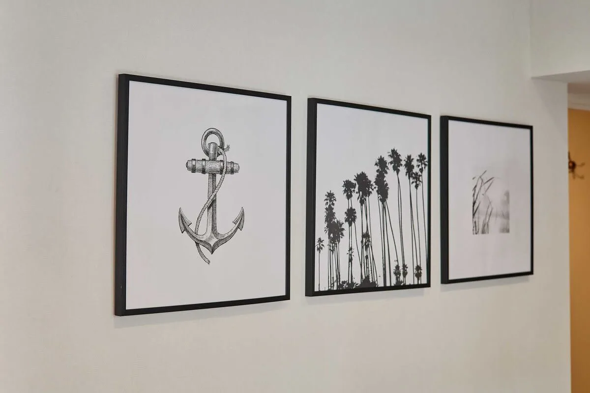 Three framed prints hang on a white wall, including an anchor and palm trees.