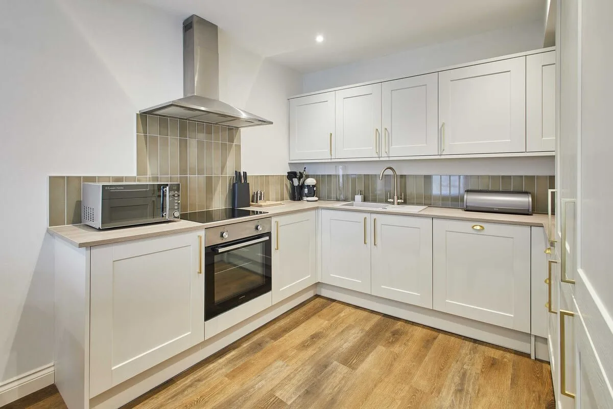 A modern kitchen with white cabinets, a built-in oven, and wood-look flooring.