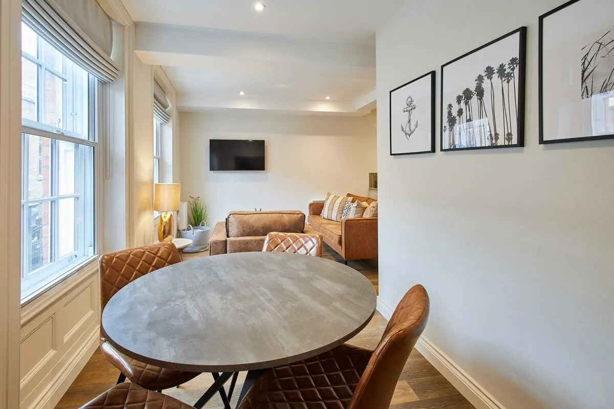 A dining area with a round table beside large windows and framed wall art.