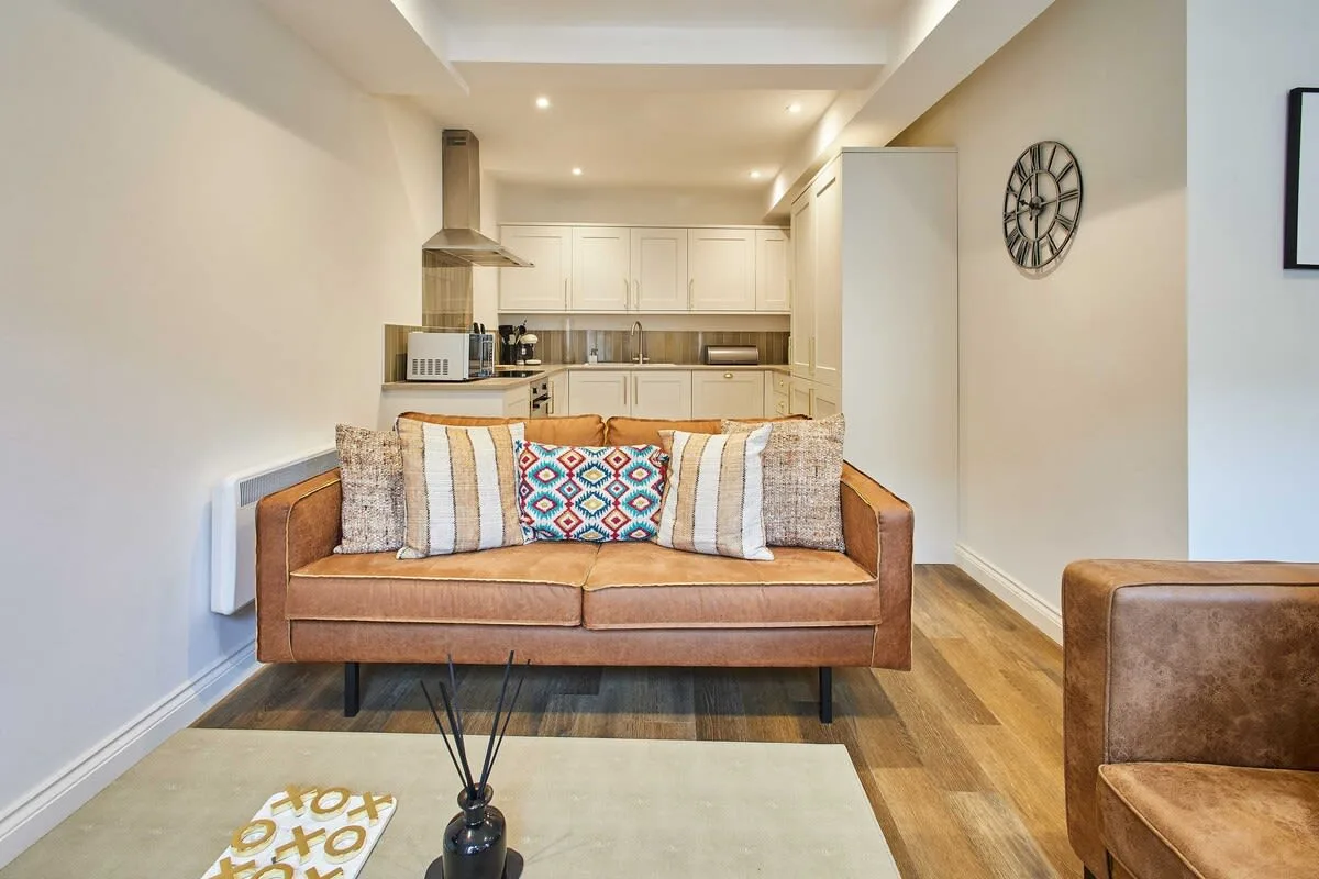 A living room with a brown sofa and an open kitchen behind it.