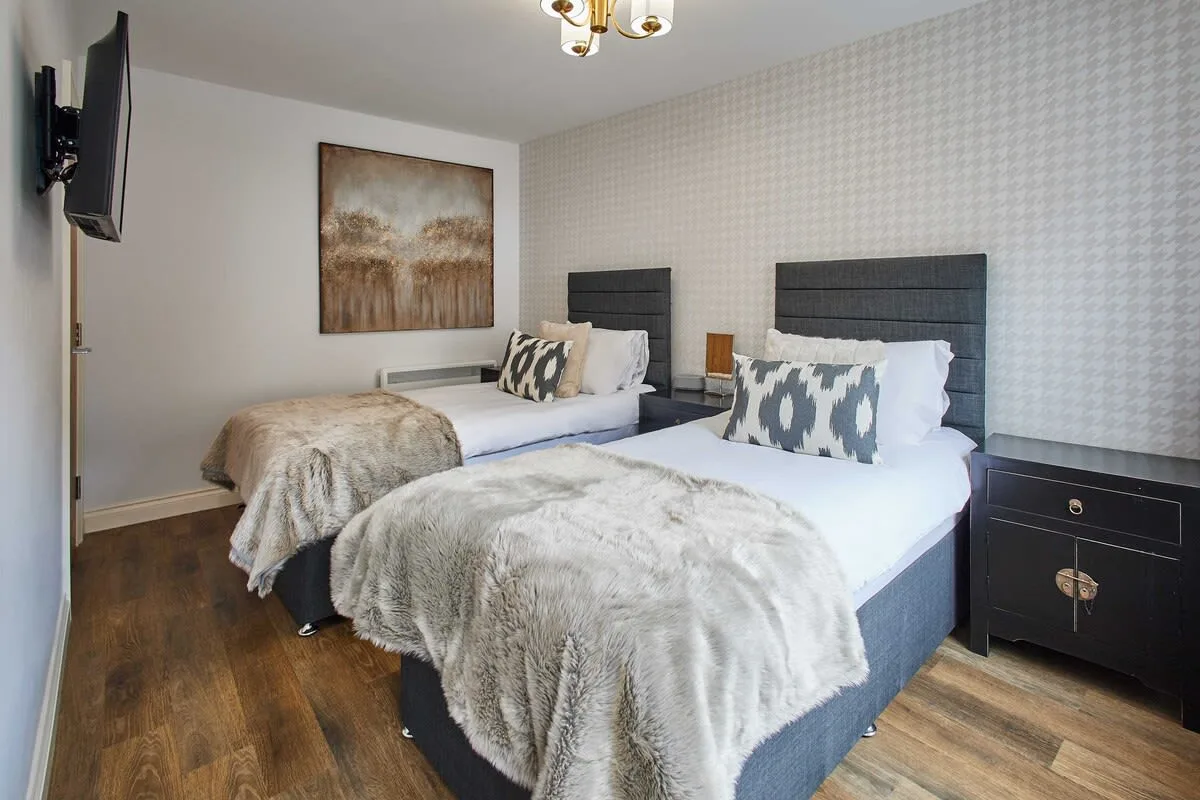 A bedroom with two beds, patterned pillows, and framed wall art.