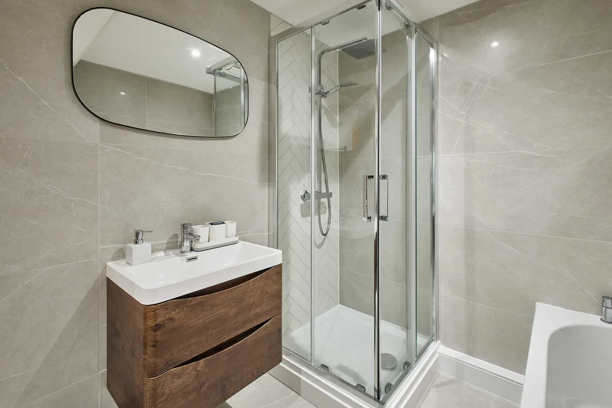 A tiled bathroom with a glass shower and a wooden vanity.