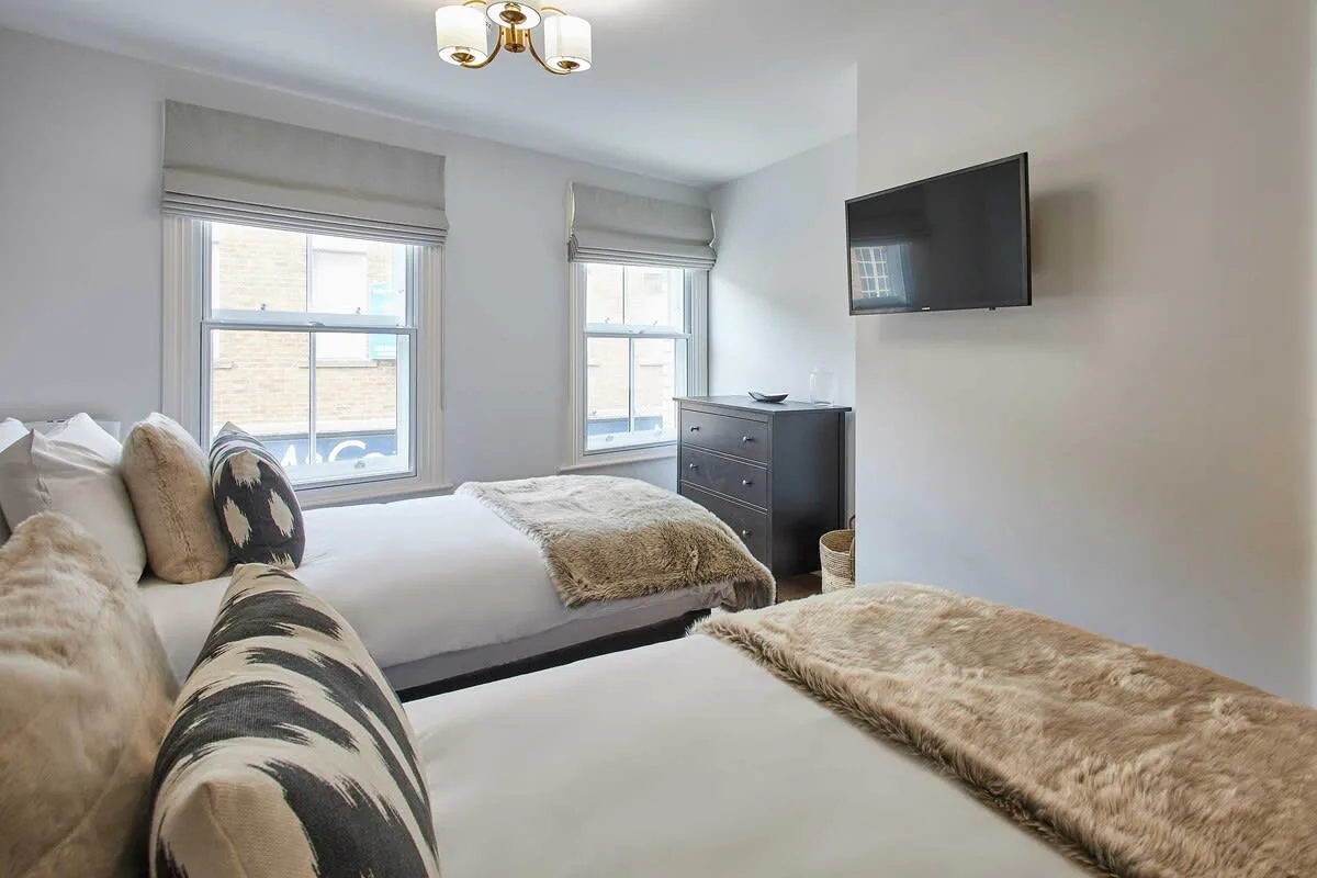 A bedroom with two beds, windows, a dresser, and a wall-mounted television.