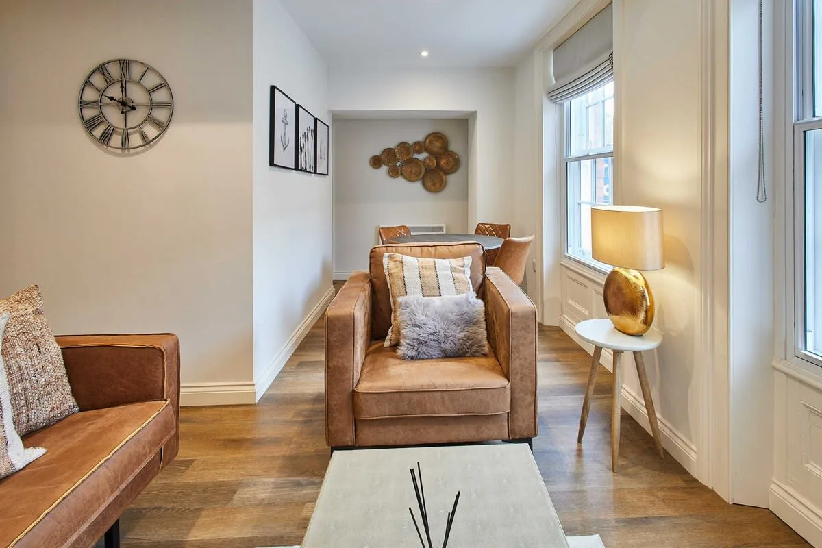 A bright sitting room with cushioned seating, framed art, and a table lamp.