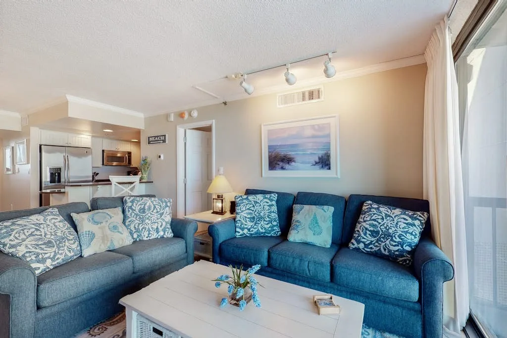 A living room with blue seating, a coffee table, and an open kitchen.