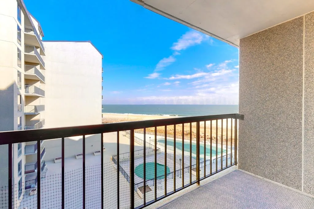 A balcony overlooks the ocean and a neighboring building.