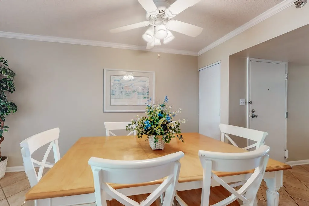 A dining area with a wooden table, white seating, and a floral centerpiece.