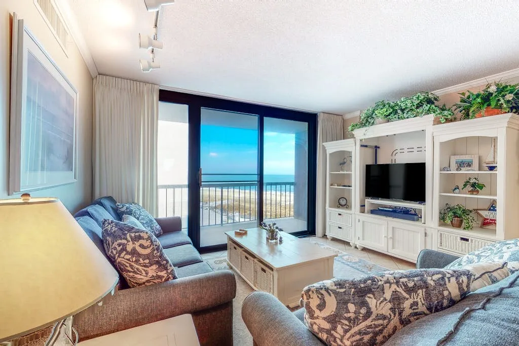 A living room with seating, a television, and glass doors opening onto a balcony.
