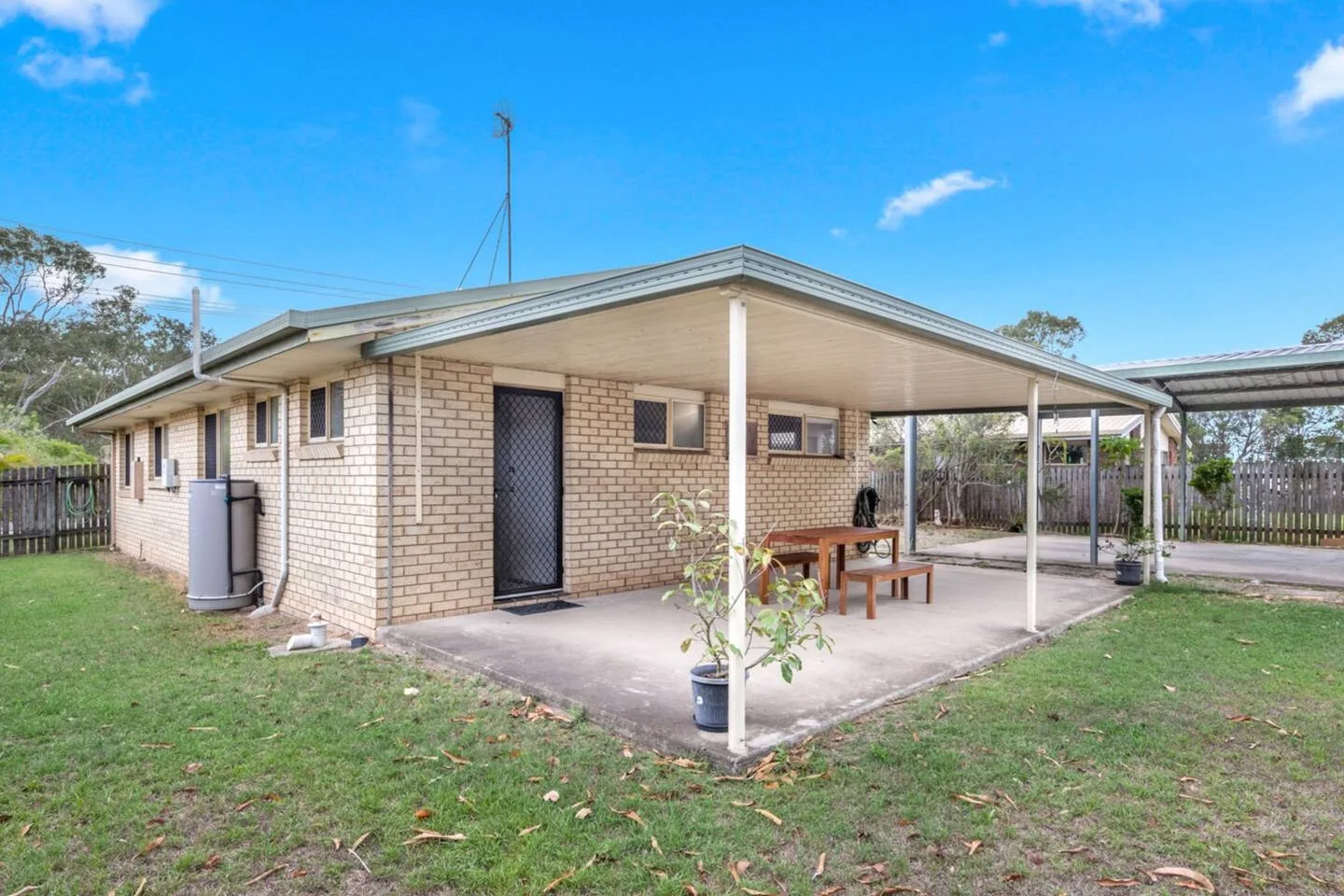 A brick house opens onto a covered patio with a small table and surrounding grass.