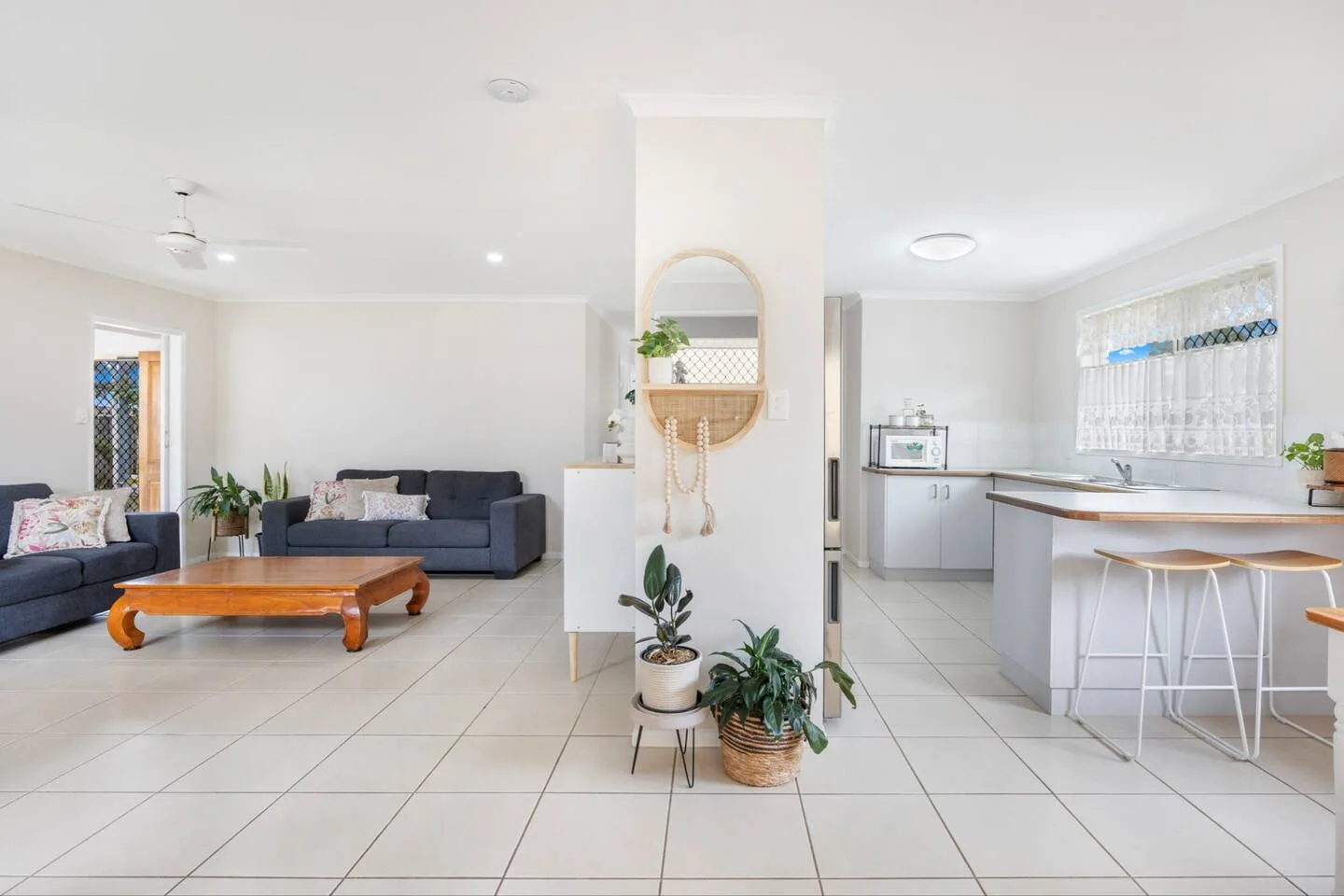 An open-plan living room and kitchen with tiled floors and a central peninsula.