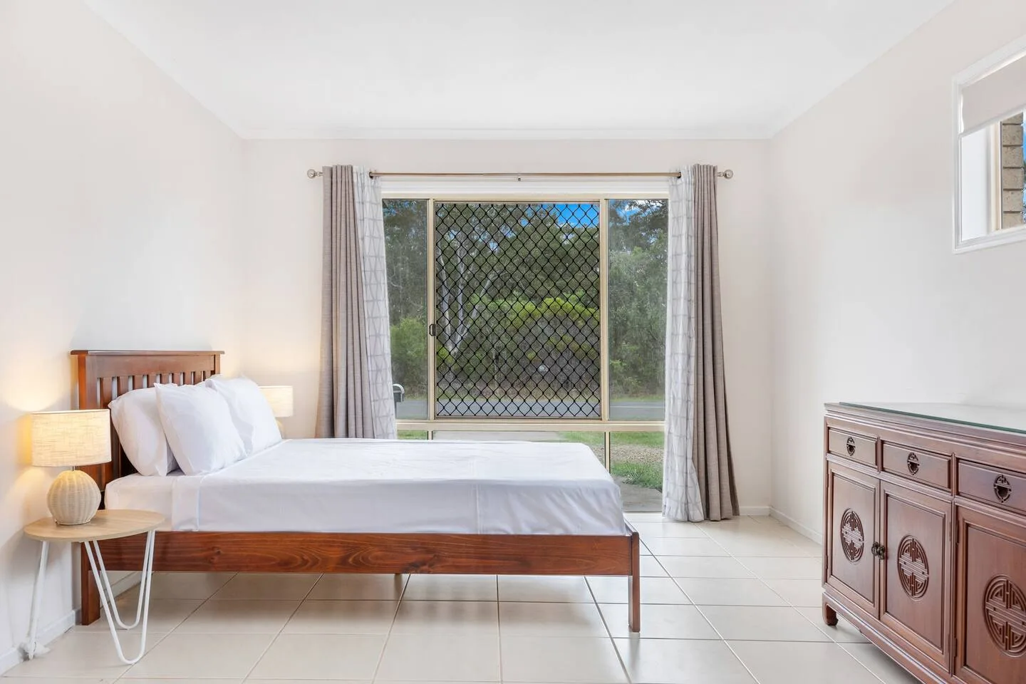 A bright bedroom with a bed, bedside table, and curtained glass doors.