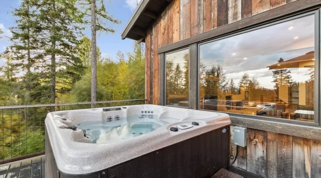 An outdoor hot tub sits beside a wood-clad building, overlooking trees.