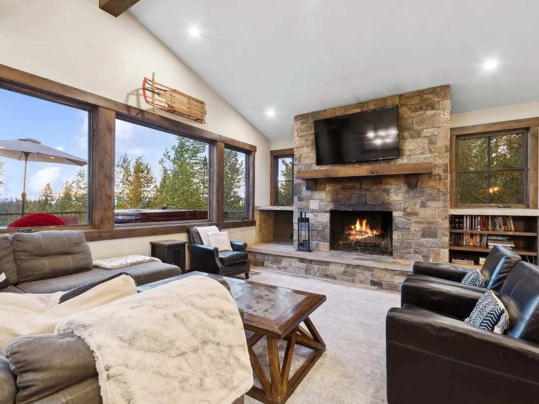 A living room with seating, a stone fireplace, and large windows.