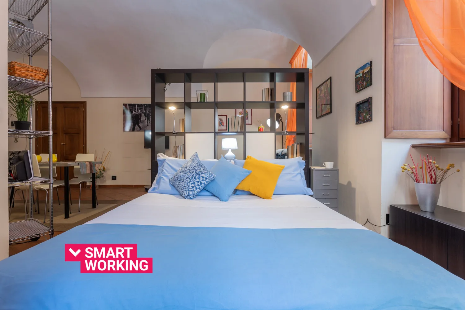 Un dormitorio con una cama y cojines de colores frente a un separador de ambientes.