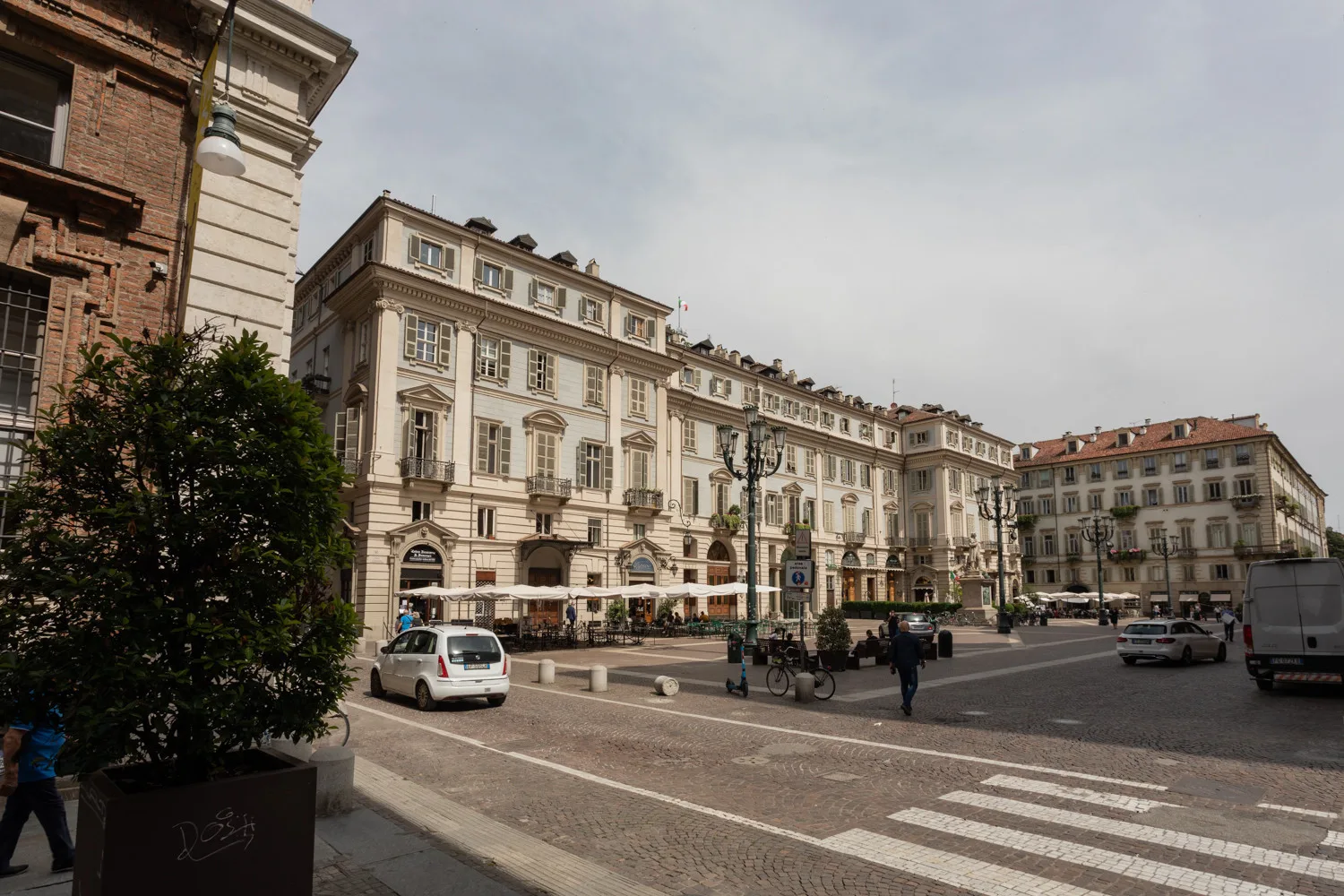 Una plaza urbana rodeada de edificios ornamentados de varias plantas, con un paso de peatones en primer plano.